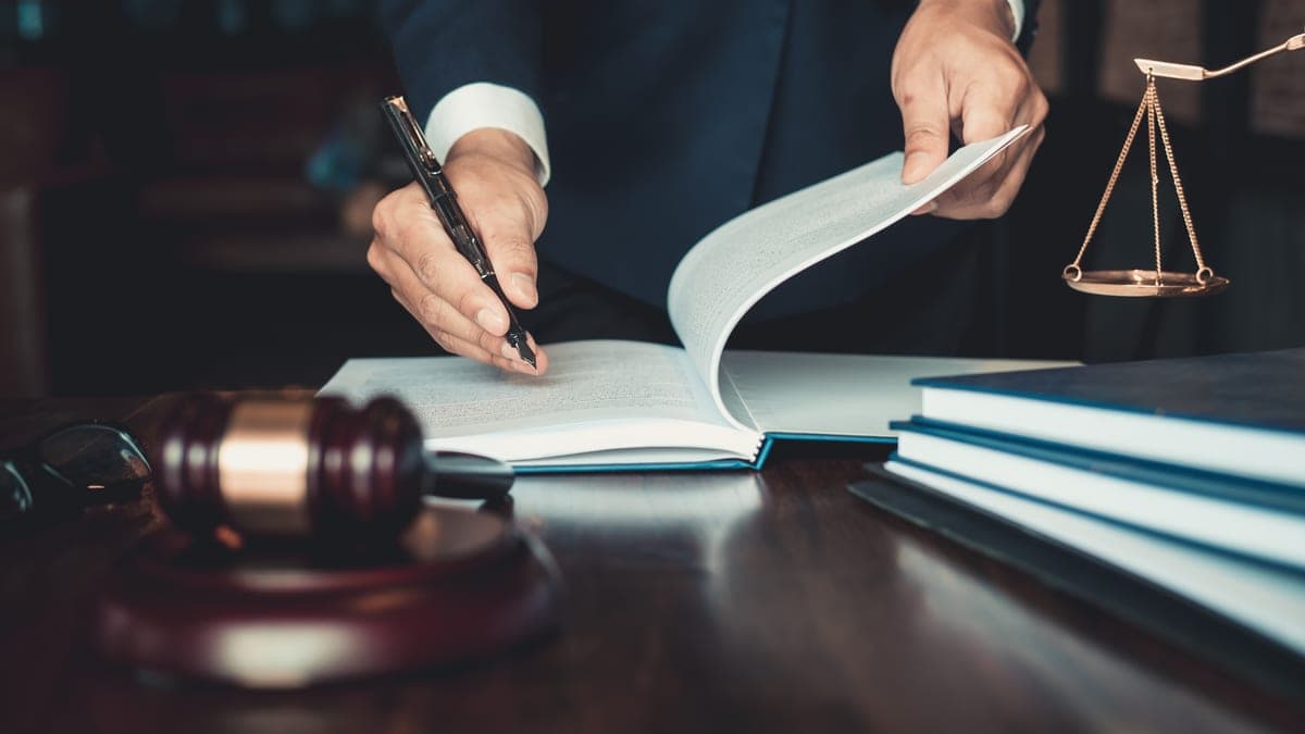 Jurist blättert ein Vertragsdokument am Schreibtisch mit Richterhammer und Waage, Sinnbild für die rechtliche Prüfung von Beraterverträgen