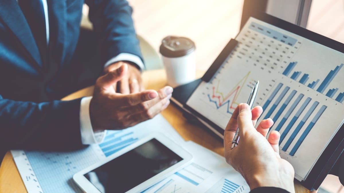 Zwei Geschäftsleute besprechen Diagramme und Berichte mit Tablet am Besprechungstisch, Sinnbild für die Arbeitsbeziehung zwischen Unternehmer und Berater