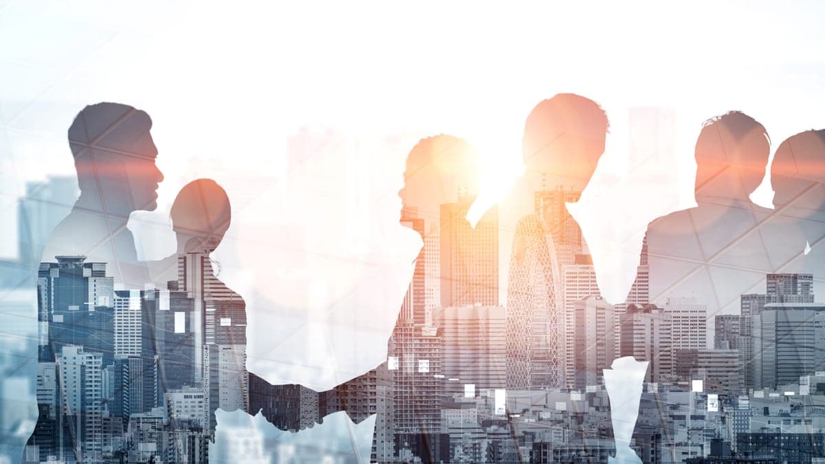 Silhouetten von Geschäftsleuten mit Handschlag als Doppelbelichtung über einer Stadtsilhouette, Sinnbild für Unternehmensübergaben im Mittelstand
