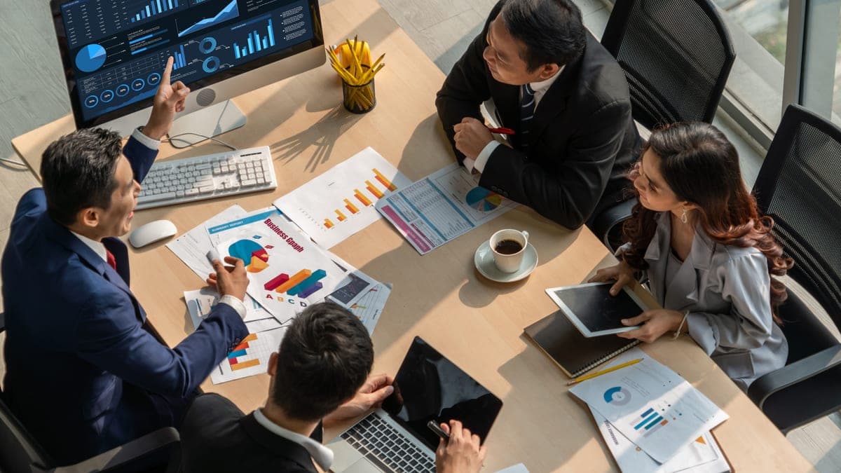 Business-Team analysiert Diagramme auf Monitor und Ausdrucken am Besprechungstisch von oben, Sinnbild für die Erfolgsmessung von Beratungsprojekten
